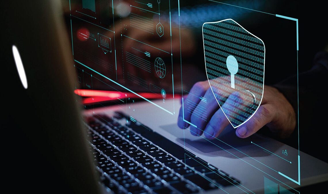 A close-up of a laptop with a blue glowing shield graphic, representing online security, data privacy, or cybersecurity measures.