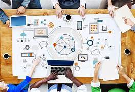 A top-down view of a modern office meeting, showcasing a diverse team working together on a strategic plan visualized through interconnected digital symbols on a large paper spread.
