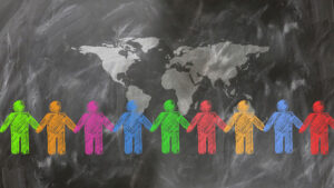 A visual representation of global unity and collaboration, showing stylized people in various colors holding hands beneath a world map on a textured dark surface.