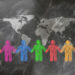 A visual representation of global unity and collaboration, showing stylized people in various colors holding hands beneath a world map on a textured dark surface.