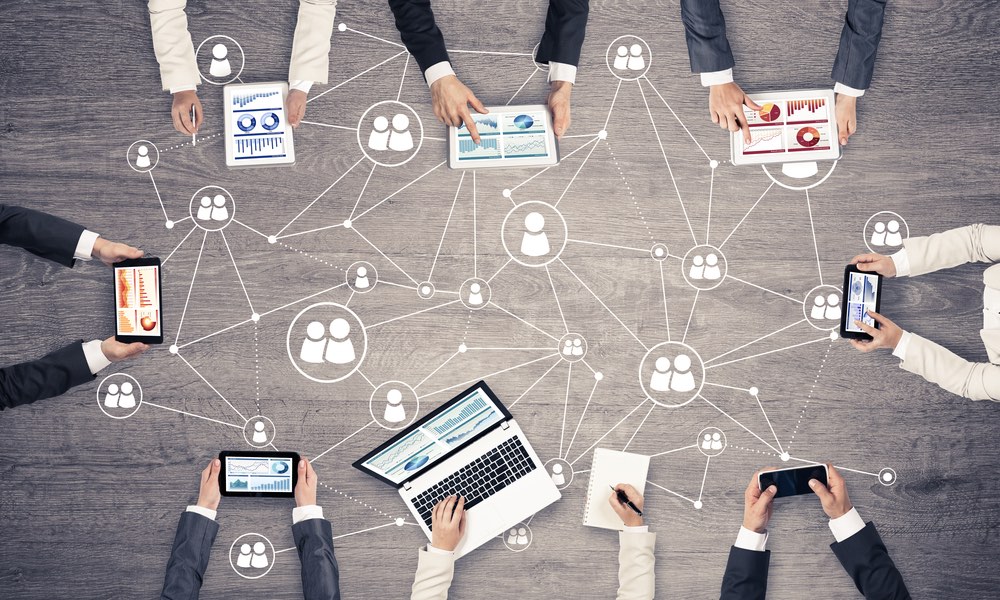 A top-down view of a collaborative meeting, showing various digital devices and a hand-drawn social network or team structure on a wooden surface.